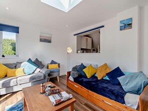A modern living room with a sofa, armchair, and coffee table, a skylight, a view of the outdoors, and a kitchen area. - 3 Bed in Saundersfoot (oc-83465) (Saundersfoot)