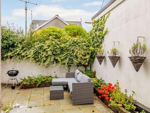 A patio with a grey sofa set, a small table, and a barbecue grill. - 5 Bed in Tenby (oc-83907) (Tenby)