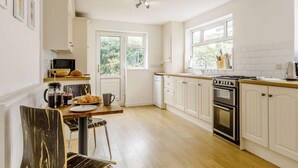 A kitchen with white cabinets, a stove, a sink, and a window. - 5 Bed in Tenby (oc-83907) (Tenby)
