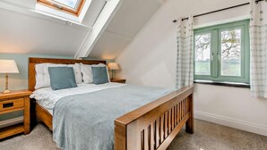 A bedroom with a sloped ceiling, a bed with a wooden headboard, a nightstand, a window with curtains, and a skylight. - 2 Bed in Narberth (oc-72864) (Whitland)