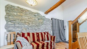 Una habitación acogedora con pared de piedra, un sofá a rayas, un banco de madera y una escalera.