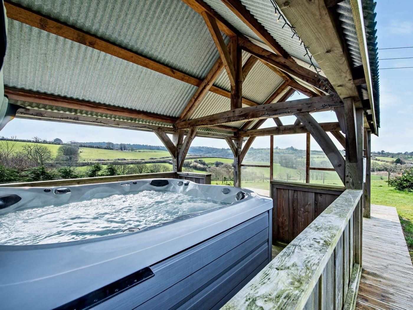 A hot tub under a wooden structure with a view of a green landscape.