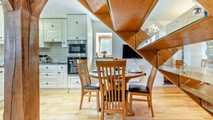 Una cocina moderna con armarios blancos, una mesa de comedor con sillas y una escalera de madera.