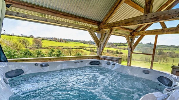 Een hottub met een houten constructie en uitzicht op groene velden.