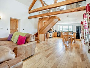 A spacious living area with a wooden staircase, a sofa with colorful cushions, a dining table, and a kitchen in the background. - 1 Bed in Narberth (oc-72867) (Whitland)
