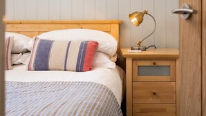 Uma cama com roupa de cama listrada, um abajur e uma mesinha de cabeceira de madeira com gavetas.