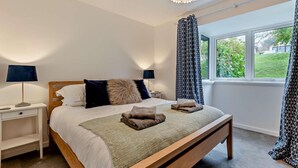 Ein Schlafzimmer mit einem hölzernen Bett, einem Nachttisch, einer Lampe und einem Fenster mit Vorhängen.