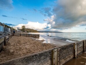 A beach with a wooden walkway, a dog running along the shore, and a cloudy sky. - 2 Bed in Saundersfoot (oc-fb271) (Saundersfoot)