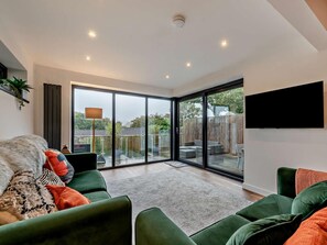 A modern living room with a green sofa, a flat-screen TV, and a large sliding glass door leading to a backyard. - 2 Bed in Saundersfoot (oc-fb271) (Saundersfoot)