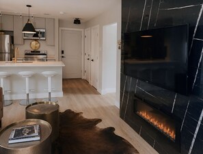 A modern kitchen with a central island, a fireplace, and a bar area with stools. - Modern Luxe 2BR + Office Bordering Highland Park (Dallas)