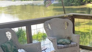 Un balcón con sillas de mimbre, una bandera y vistas al río.