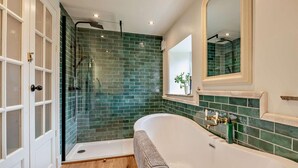 Ein Badezimmer mit einer freistehenden Badewanne, einer Duschkabine aus Glas und einer Wand mit grünen Fliesen.