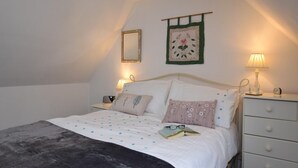 Una camera da letto con un letto, cuscini, un comodino con una lampada, una cassettiera e uno specchio fissato al muro.