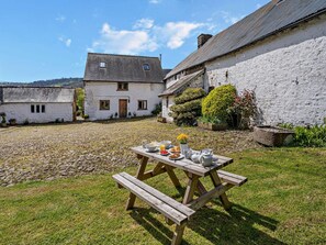 A courtyard with a picnic table set up with food and drinks, surrounded by white buildings with stone walls.