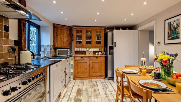 Una cocina con armarios de madera, estufa a gas, microondas y un comedor con mesa y sillas.