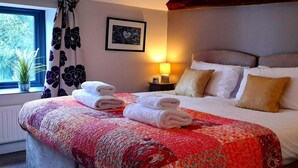 Una habitación de hotel con cama, ventana con cortinas, mesita de noche con lámpara y un cuadro enmarcado en la pared.