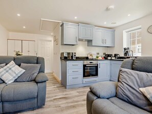 A modern kitchen with grey cabinets, a microwave, and an oven. There are two grey sofas with cushions. - 2 Bed in Looe (oc-90966) (Trelawne)