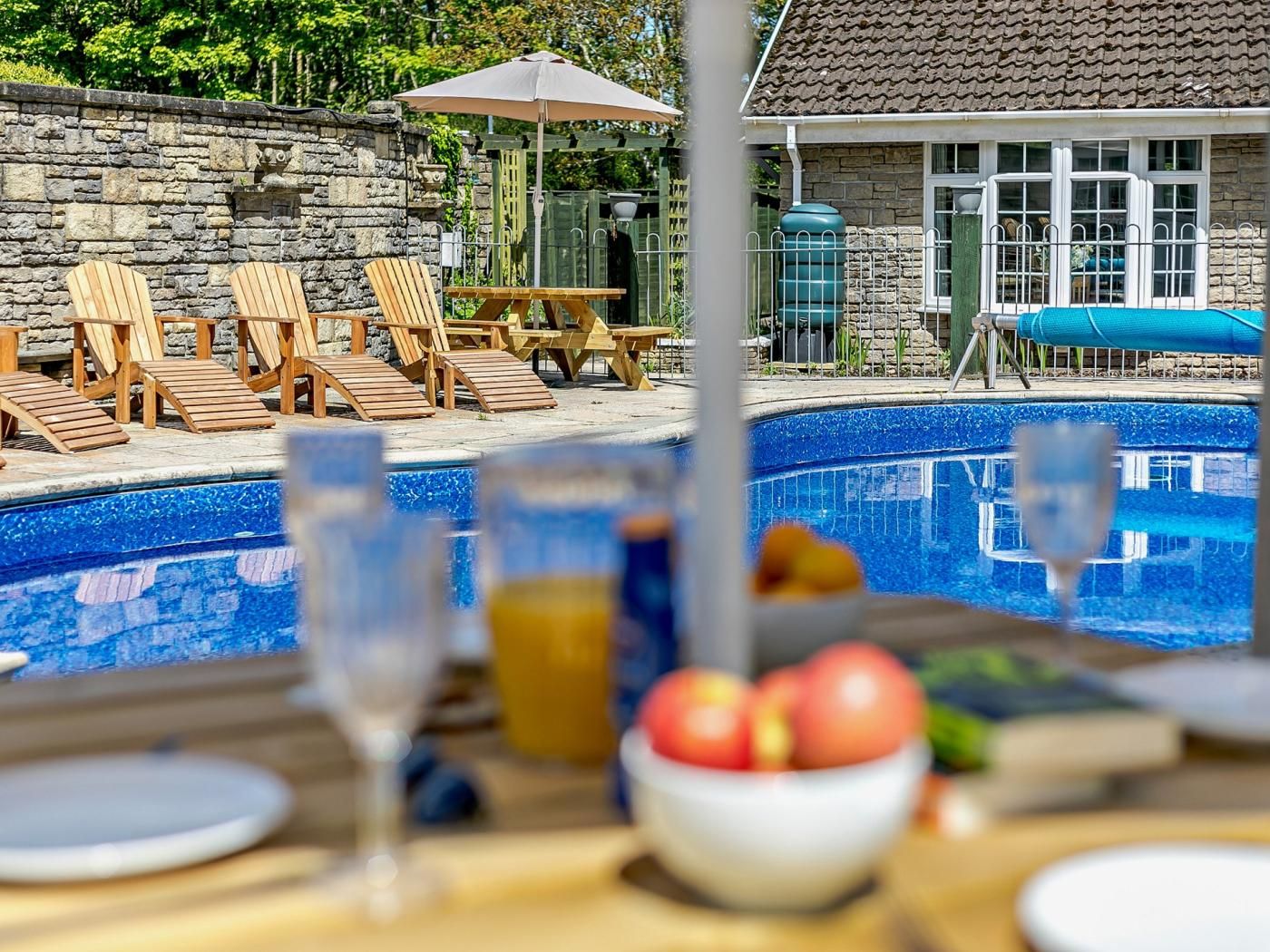 A poolside dining area with lounge chairs, a table, and a view of a swimming pool.