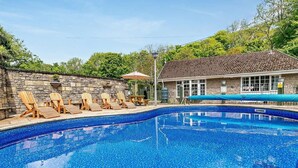 Uma piscina com espreguiçadeiras, um muro de pedra e um edifício com telhado de azulejos.