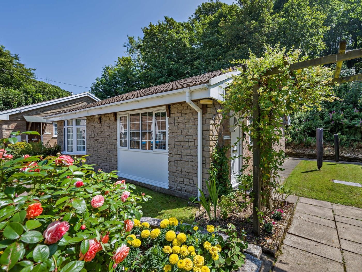 A residential building with a stone facade, a tiled roof, and a garden with flowers and shrubs.