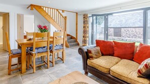 A living room with a wooden dining table, chairs, a sofa, a staircase, and a large window. - 3 Bed in Ratlinghope (oc-79238) (Ratlinghope)