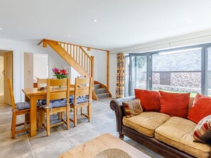 A living room with a wooden dining table, chairs, a sofa, a staircase, and a large window. - 3 Bed in Ratlinghope (oc-79238) (Ratlinghope)