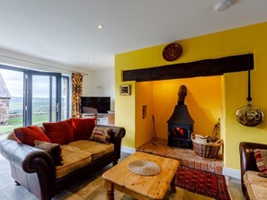 A living room with a fireplace, a sofa, a coffee table, and a view through a glass door. - 3 Bed in Ratlinghope (oc-79238) (Ratlinghope)