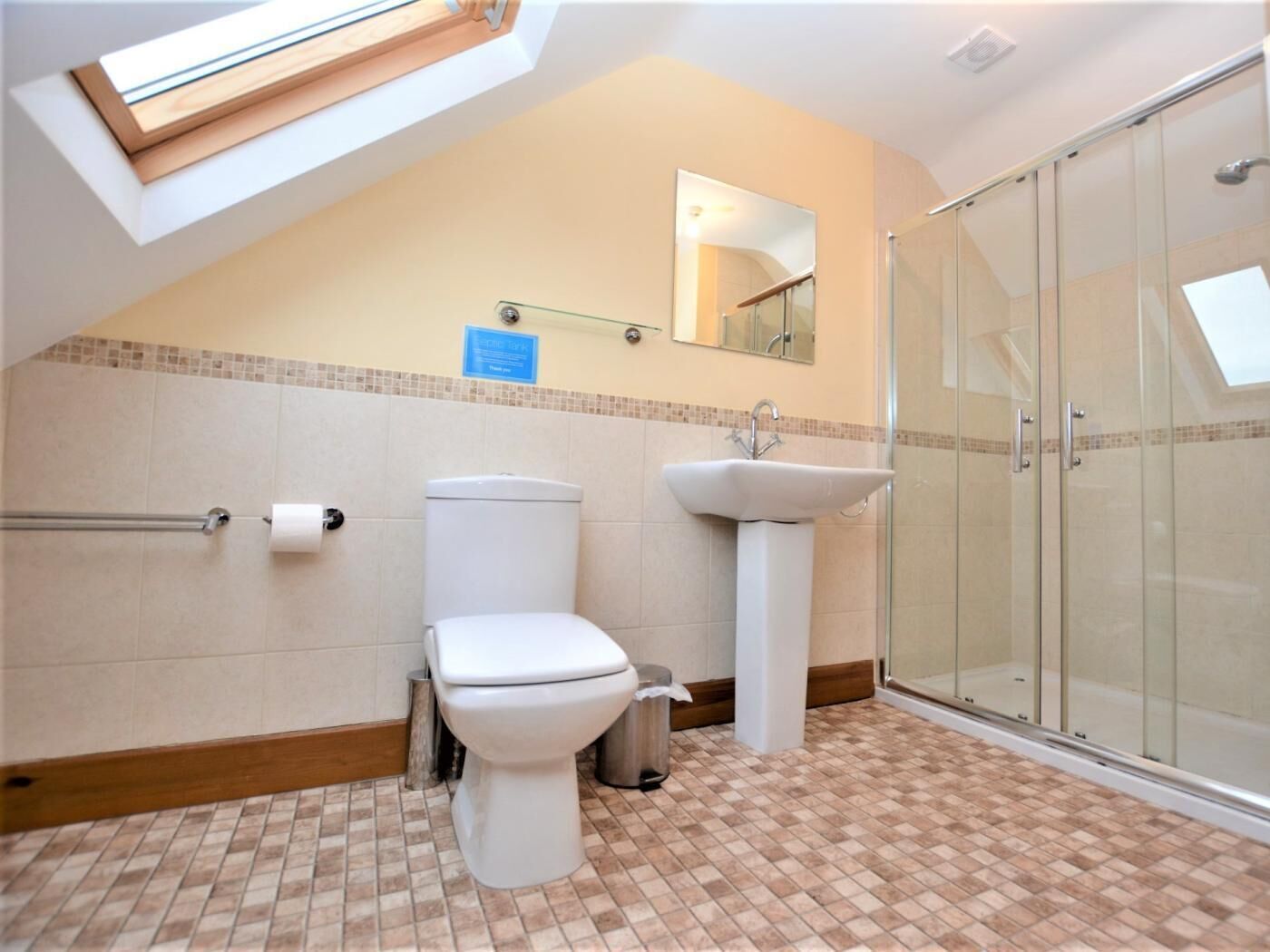 A bathroom with a skylight, toilet, sink, and glass shower enclosure.