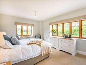 A bedroom with a bed, bedside tables, a dresser, and large windows with a view of greenery. - 4 Bed in Wrexham (oc-87675) (Pont-y-blew)