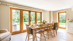 A dining area with a wooden table and chairs, large sliding glass doors leading to a garden, and a white cabinet to the right. - 4 Bed in Wrexham (oc-87675) (Pont-y-blew)