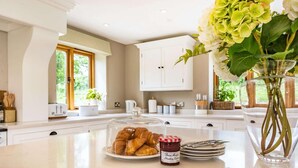 A kitchen with a marble countertop, a glass display case with croissants, a jar of strawberry jam, and a vase with flowers. - 4 Bed in Wrexham (oc-87675) (Pont-y-blew)