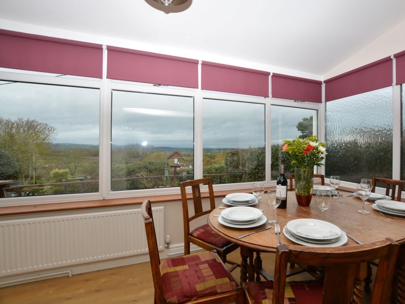 A dining area with a table set for four, large windows with a view of the countryside, and a radiator below the windows.