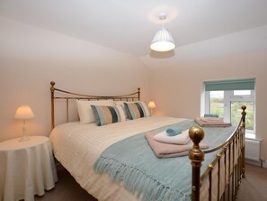 A neatly made bed with a headboard, two bedside tables with lamps, a window with a view, and a hanging light fixture. - 3 Bed in Shrewsbury (oc-40595) (Pontesbury)