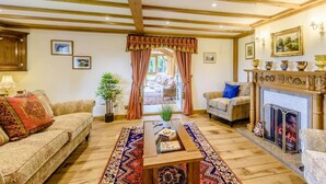 A living room with a fireplace, wooden beams, a sofa, a coffee table, and a view through a doorway. - 6 Bed in Bala (oc-80348) (Fron-goch)