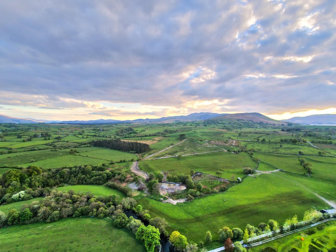 Une vue panoramique d’un paysage rural, avec des collines ondulantes, des champs et une route sinueuse.