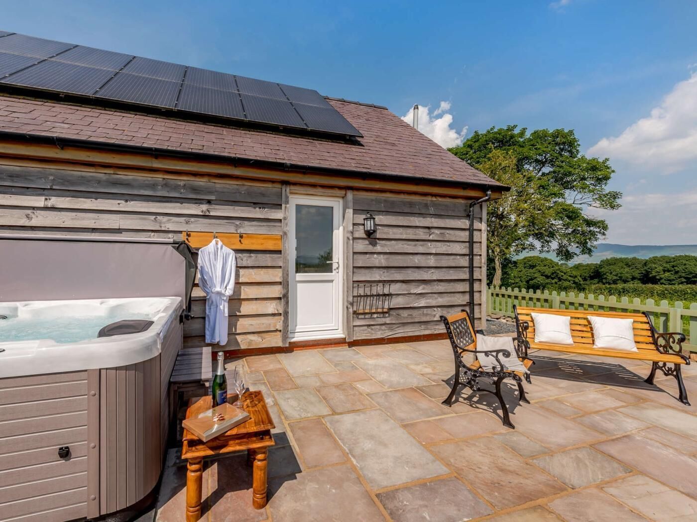 A wooden cabin with a hot tub, a bench, and a table with a bottle and glass.