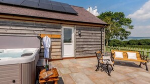 A wooden cabin with a hot tub, a bench, and a table with a bottle and glass. - 1 Bed in Ruthin (oc-83640) (Llanfwrog)