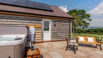 A wooden cabin with a hot tub, a bench, and a table with a bottle and glass.