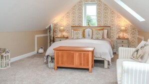 A bedroom with a sloped ceiling, a bed with matching headboard, bedside tables with lamps, a wooden bench, and a window with a view. - 1 Bed in Ruthin (oc-83640) (Llanfwrog)