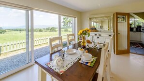 A dining area with a table set for breakfast, a view of the countryside, and a kitchen in the background. - 1 Bed in Ruthin (oc-83640) (Llanfwrog)