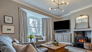Ein Wohnzimmer mit einer Couch, einem Couchtisch, einem Kamin, einem Fernseher und einem großen Fenster mit Vorhängen.