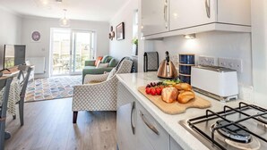 Une cuisine moderne équipée d’une cuisinière à gaz, d’une bouilloire et d’un grille-pain. On y trouve également un coin repas avec une table et des chaises, ainsi qu’un salon avec un canapé et une table basse.