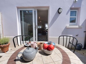 A patio with a table set for tea, a bowl of apples, and a potted plant. - 2 Bed in Tenby (oc-87494) (Tenby)