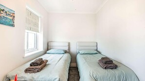 Une petite pièce propre, avec deux lits, une fenêtre et un tableau accroché au mur.
