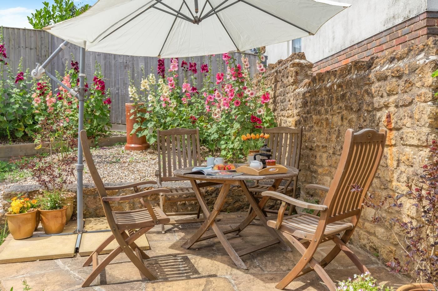 An outdoor patio with a table and chairs, surrounded by potted plants and a stone wall.