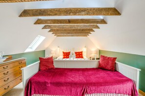 A bedroom with a sloped ceiling, a bed with a red bedspread, a dresser with drawers, and a window providing natural light.