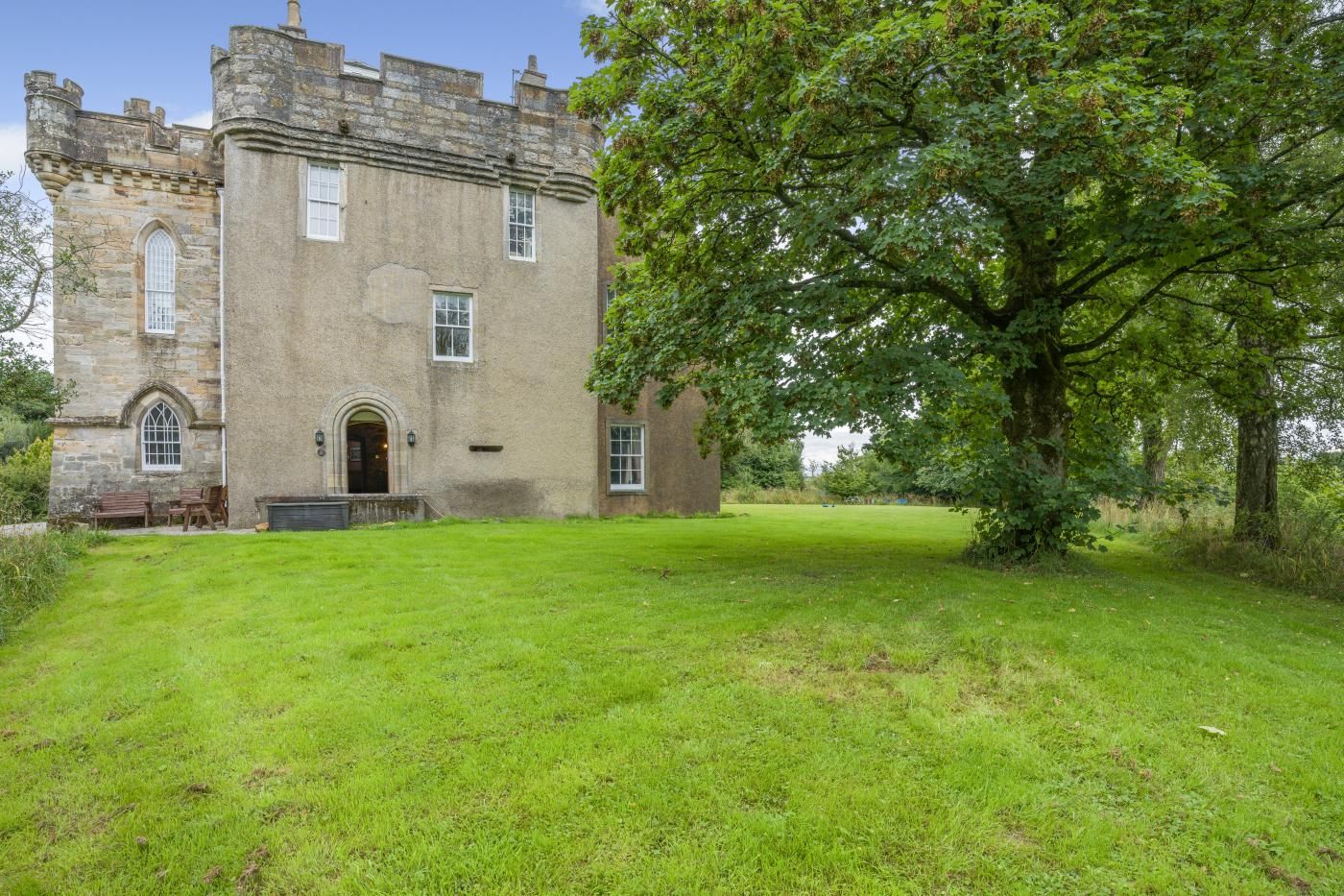 A castle with a large lawn in front, stone walls, and a prominent tree.