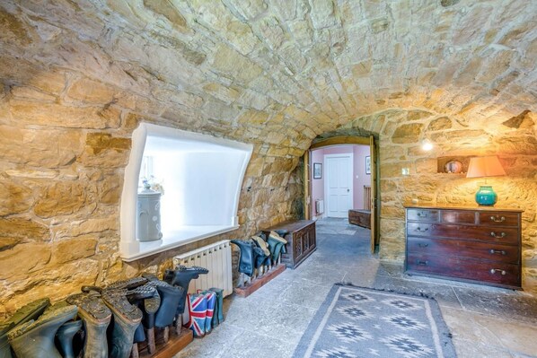 A stone-walled room with a window, a radiator, a wooden bench, a dresser, and a patterned rug.