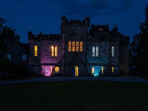 A historic building with a central arched entrance, flanked by symmetrical wings, and illuminated windows.