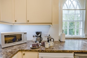 A kitchen with a microwave, coffee maker, and a window with a view of trees.